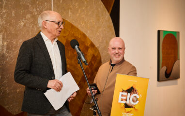 Kevin Ruck and Martin Flegg in front of a colourful artwork speaking at the launch of Exploring Internal Communication 5th edition