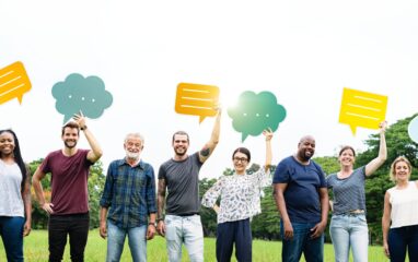 Diverse group of men and women holding speech bubbles. Men and women of various ethnicities smiling. Speech bubbles in various colors. Group of diverse people outdoors. Community and communication.